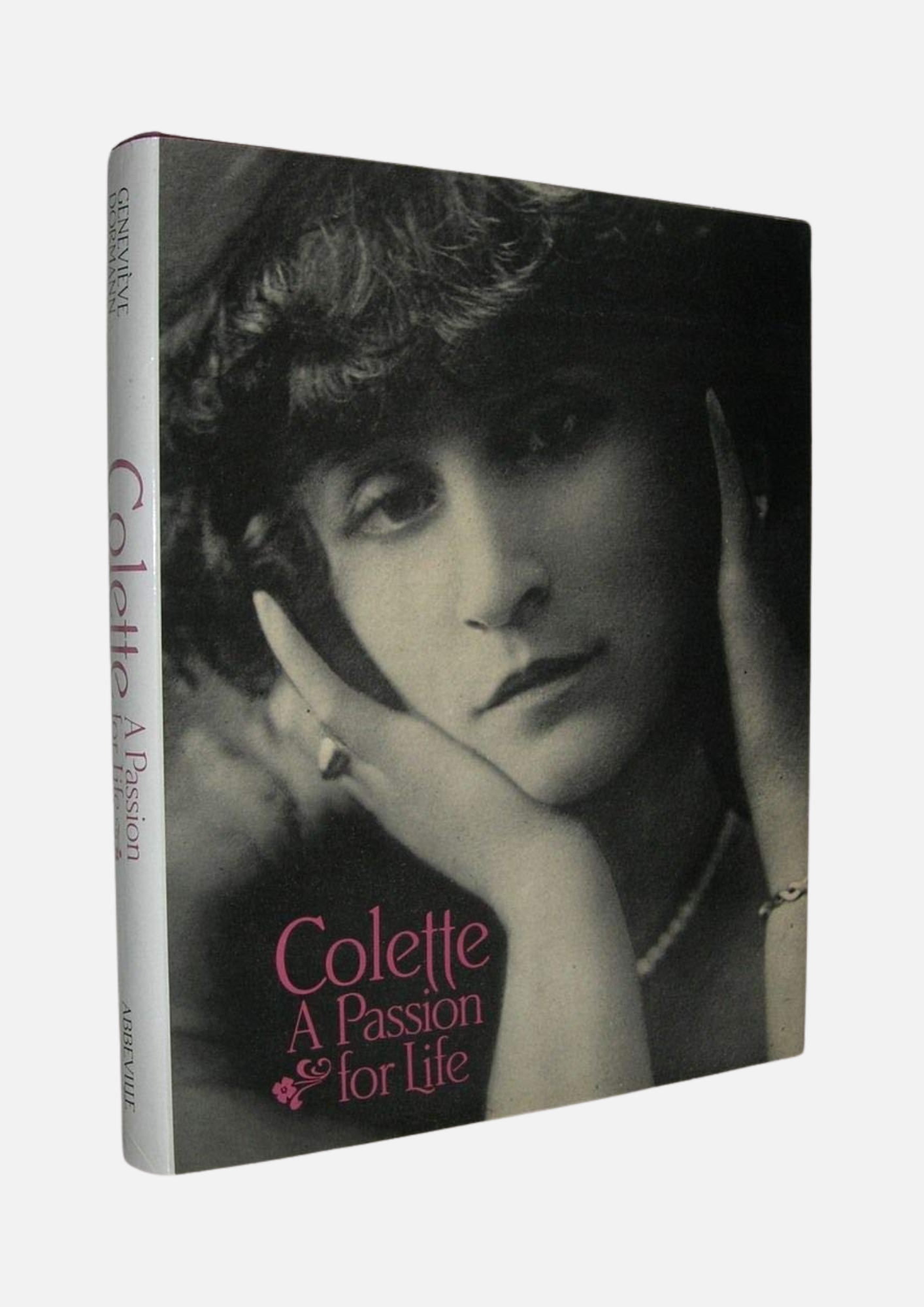 Couverture du livre "Colette: A Passion for Life", présentant une photographie en noir et blanc de l'auteure Colette. Elle est représentée de profil, avec des cheveux ondulés et une expression pensive, les mains posées sur son visage. Le titre du livre est inscrit en lettres roses sur un fond sombre, avec le mot "Colette" en haut et la phrase "A Passion for Life" en bas. Le livre est un hommage à sa vie et à son œuvre littéraire.