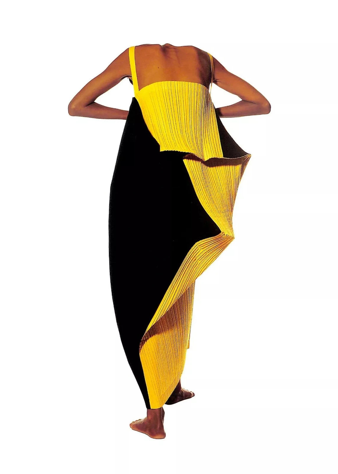 Page ouverte du livre montrant les design de Miyake à travers des photos d'Irving Penn. Photo d'une mannequin ayant penché la tête en avant, vue de dos, portant une robe plissée noir et jaune.