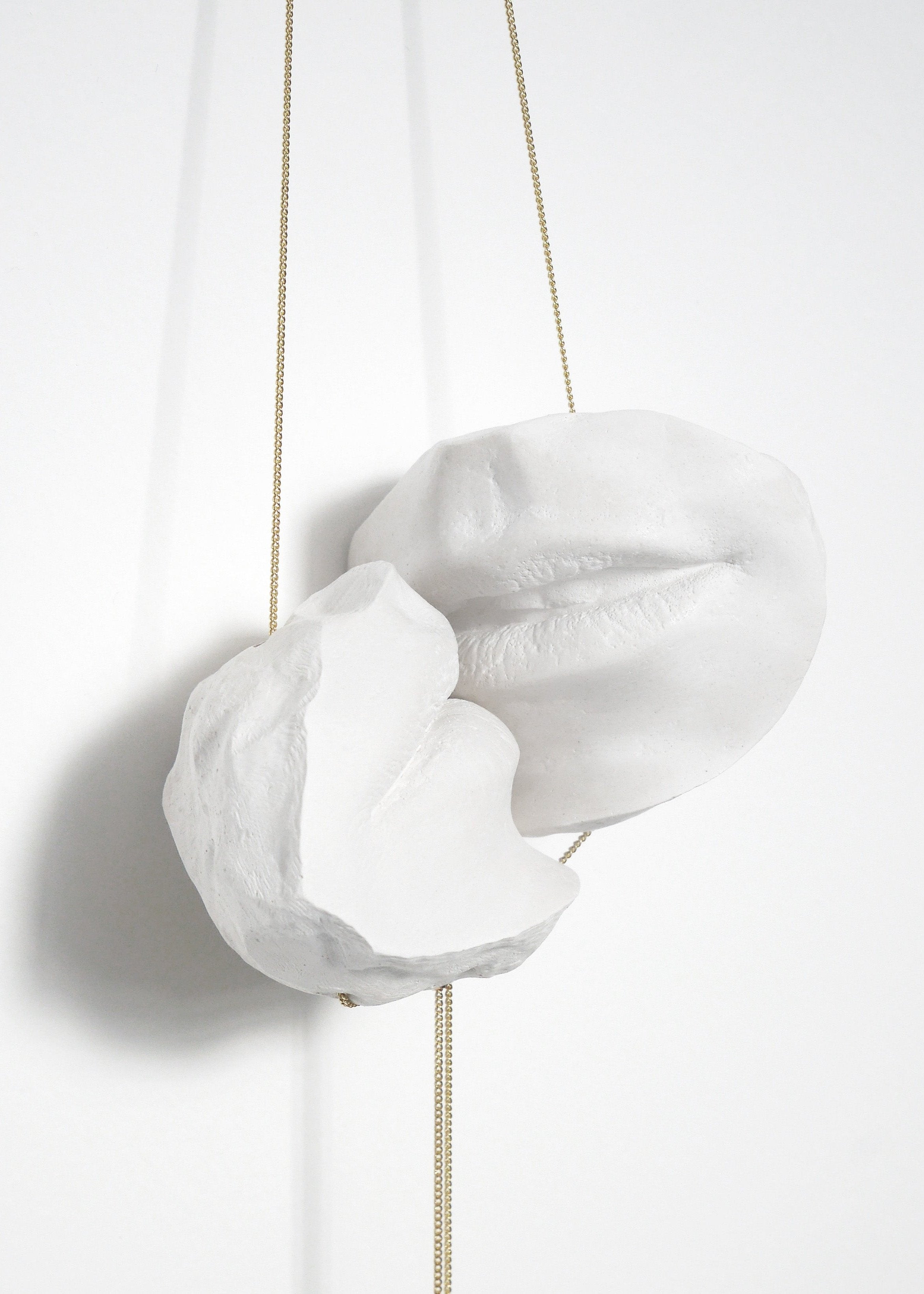 La sculpture en plâtre suspendue, avec ses deux bouches blanches et ses fils dorés délicats, est une œuvre d'art moderne et minimaliste qui joue avec la légèreté et la texture du matériau. Les formes simples et épurées créent une sensation de calme et de sérénité, tandis que la texture du plâtre ajoute une dimension tactile à l'œuvre.