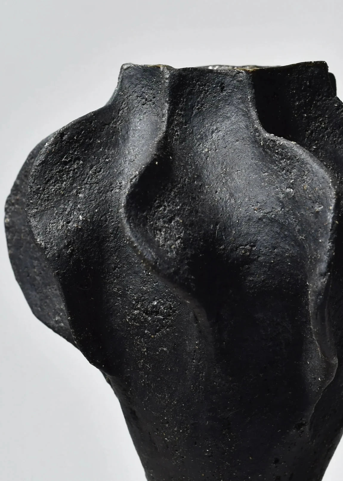 Vase contemporain en grès noir, avec une texture rugueuse et des courbes sculpturales, idéal pour une décoration d'intérieur moderne. Le design unique met en valeur l'élégance du matériau et s'intègre parfaitement dans divers styles d'aménagement.